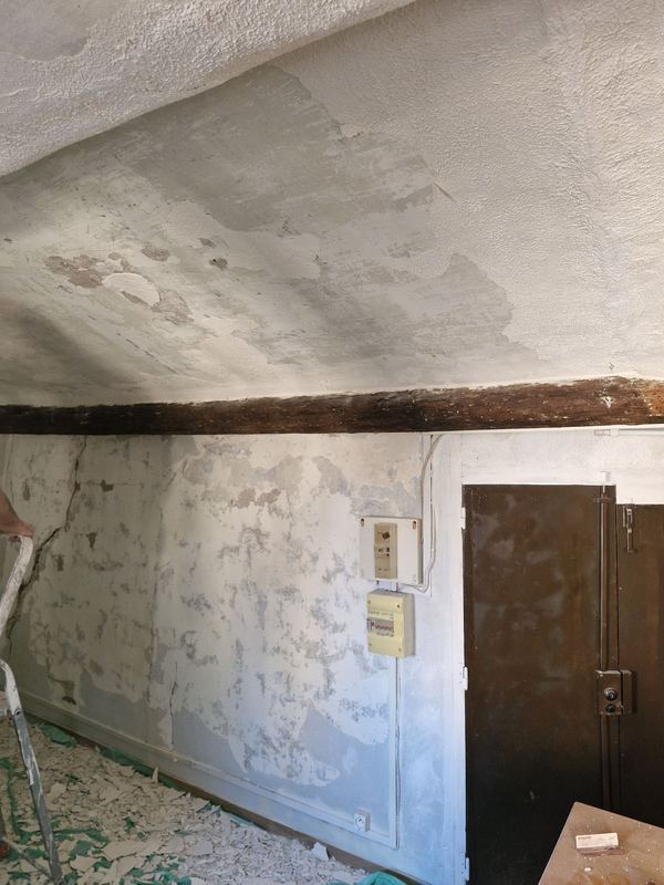 Avant : plafond et mur abîmés sous une poutre, gravats au sol